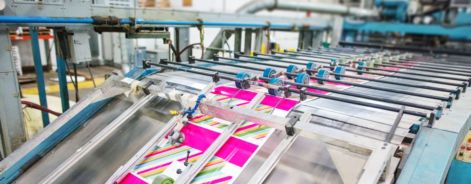 Printing machinery in action, showcasing vibrant graphic packaging with pink and colorful designs, emphasizing innovative print technology for product presentation and consumer engagement.