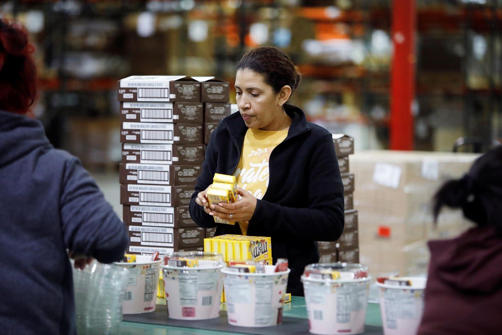 Woman assembling products in a warehouse, surrounded by buckets and boxes, illustrating TRG's co-packing and fulfillment services.