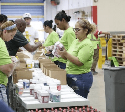 Workers in green shirts packing products into boxes at a fulfillment facility, illustrating TRG's co-packing and assembly services.