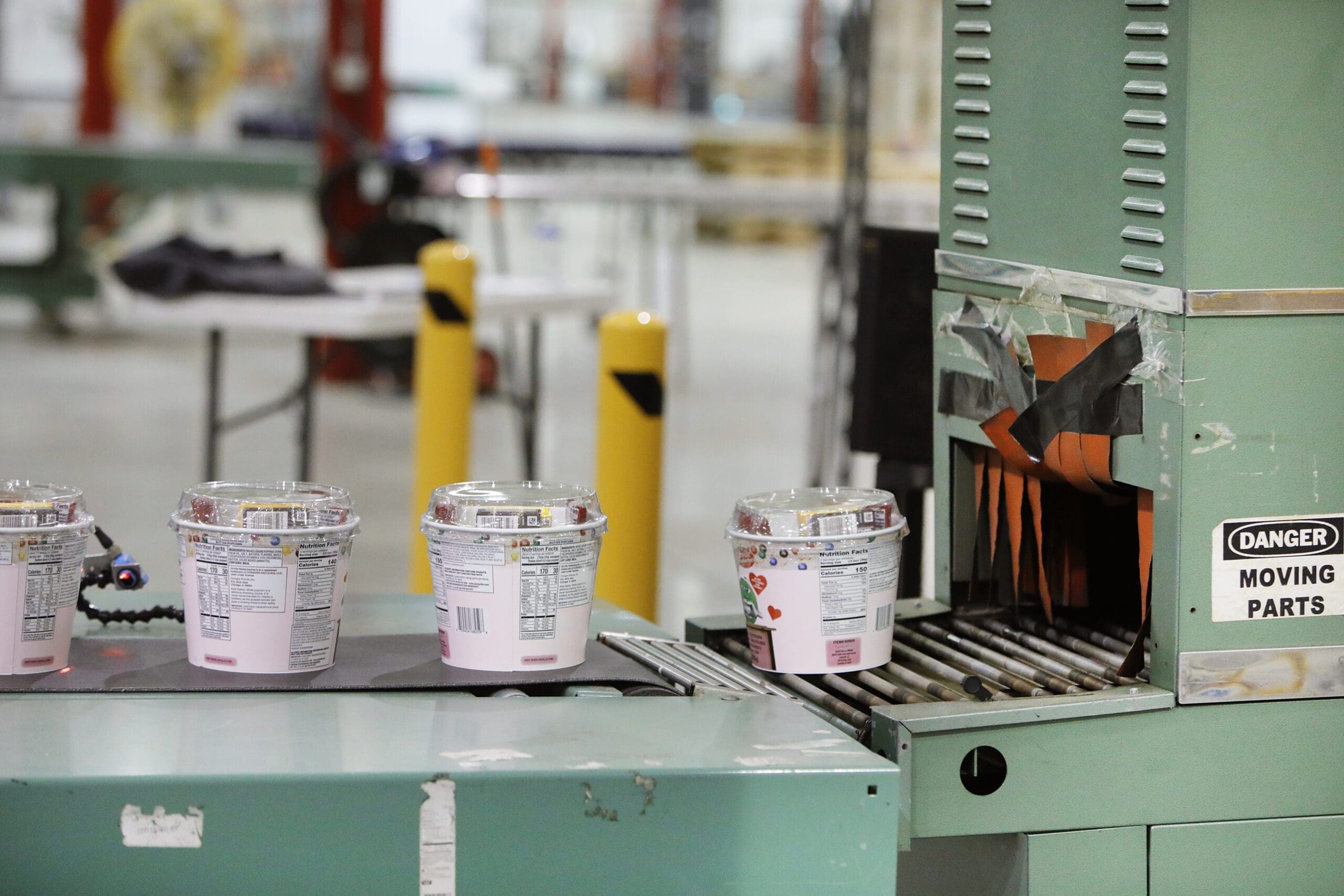 Ice cream containers on conveyor belt at co-packing facility, showcasing packaging process and equipment, emphasizing TRG's fulfillment services.