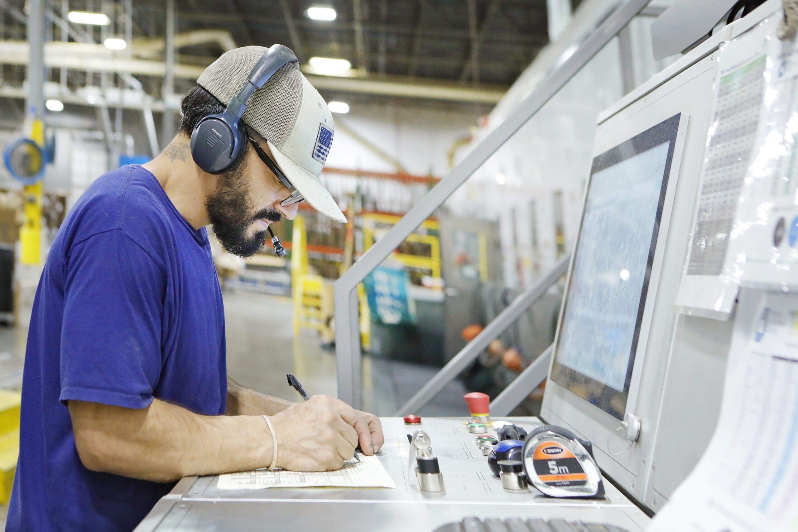 Warehouse employee using headset and taking notes at control panel in co-packing and fulfillment facility, emphasizing operational efficiency and technology integration at The Royal Group.